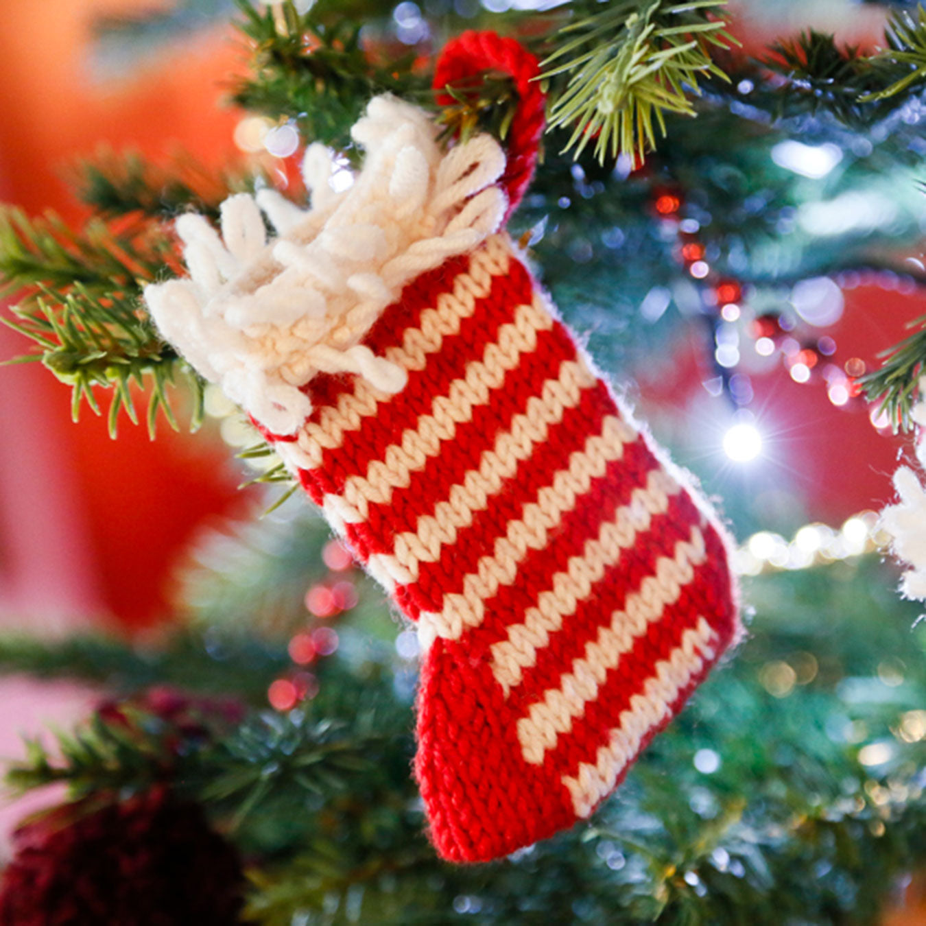 Red and white striped knitted stocking hanging on a Christmas tree.