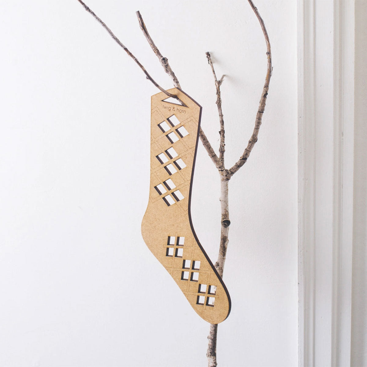Twig & Horn MDF sock blocker with argyle pattern cut out in sections for air flow hanging on a birch twig