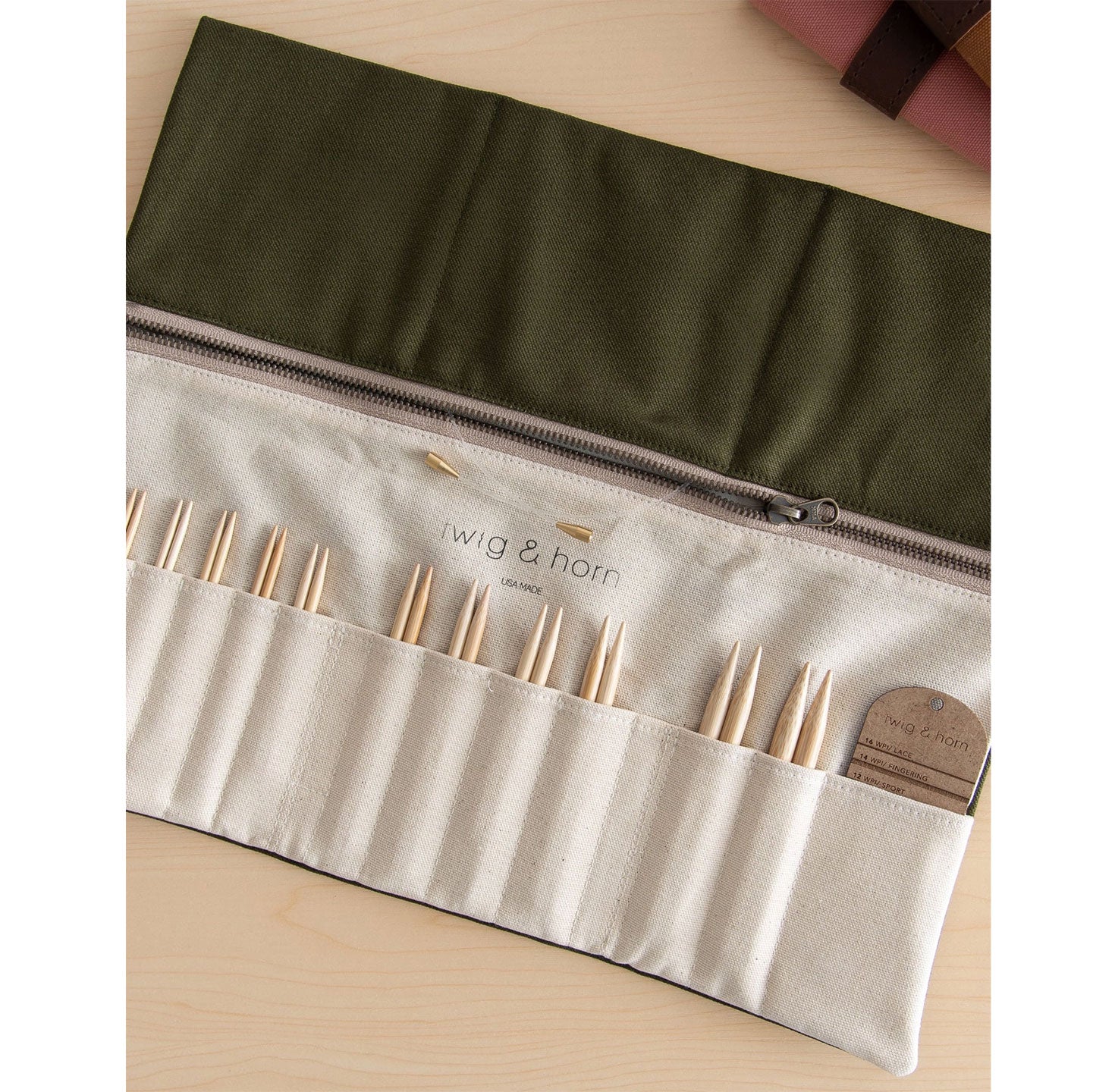 Overhead view of flat opened olive canvas interchangeable knitting needle case, tip pockets of varying size with bamboo tips on show and WPI tool in largest pocket