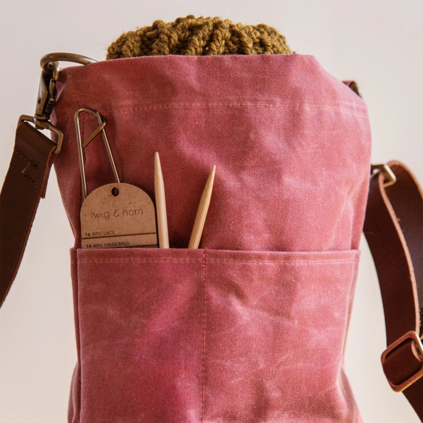 Cranberry pink bag with knitting needles and a WPI tool showing in side pocket, on a light background