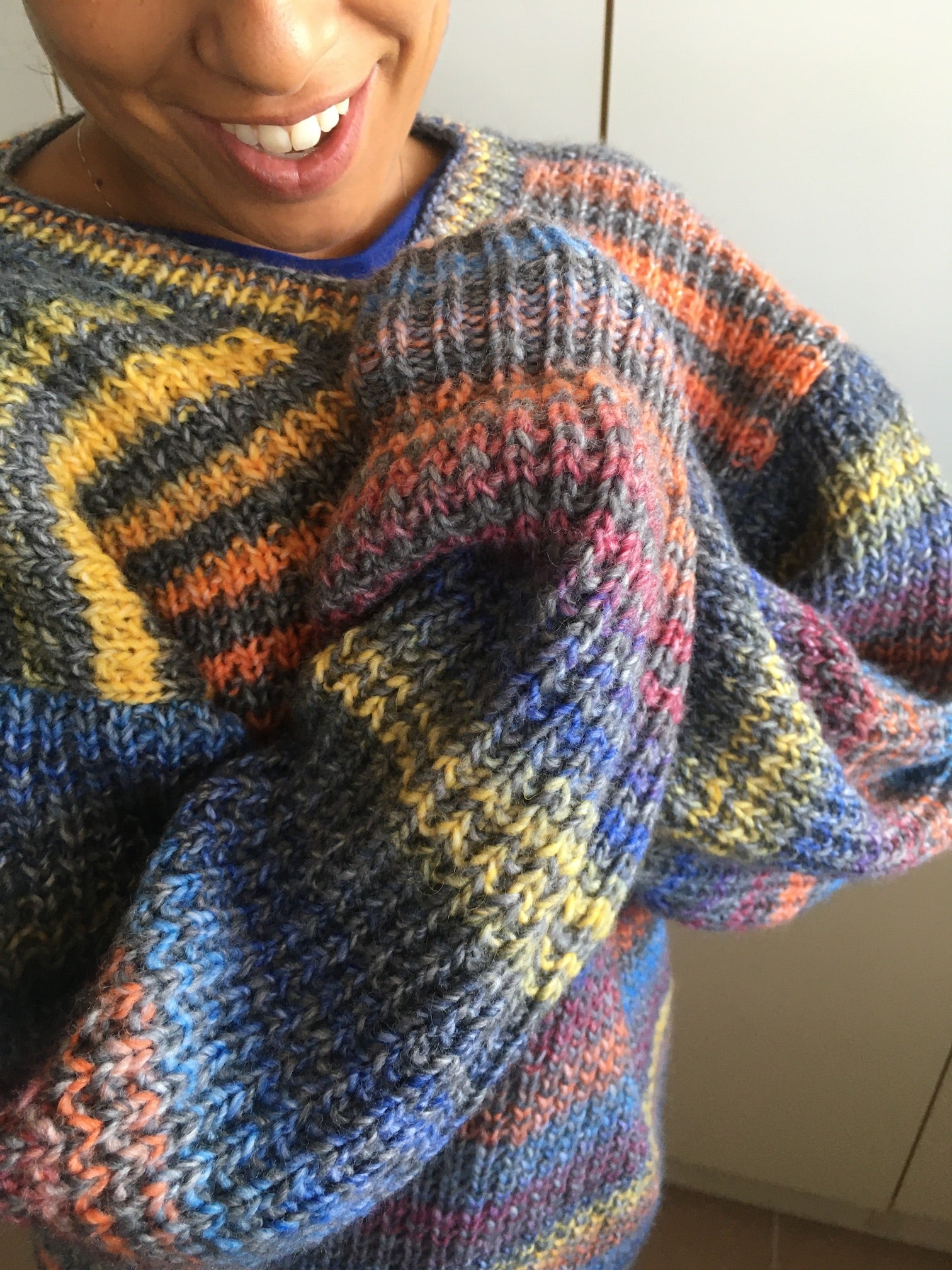 Person wearing a colourful striped sweater knitted with Adriafil's Zebrino yarn against a neutral background
